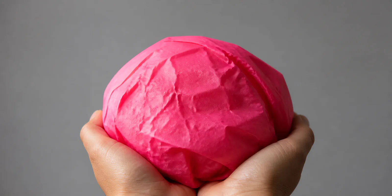 Manos sosteniendo desde abajo un envoltorio de papel seda rosa fluor