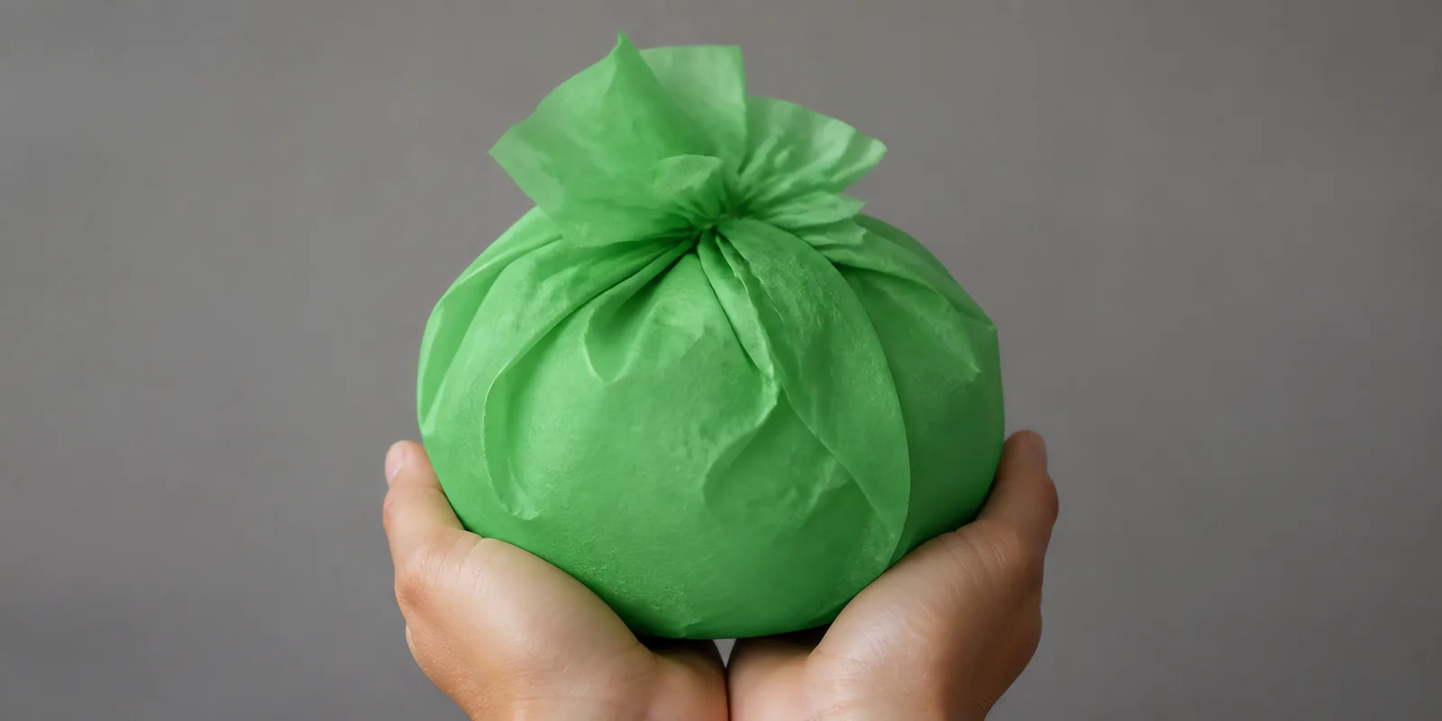Manos sosteniendo desde abajo un envoltorio de papel seda verde manzana