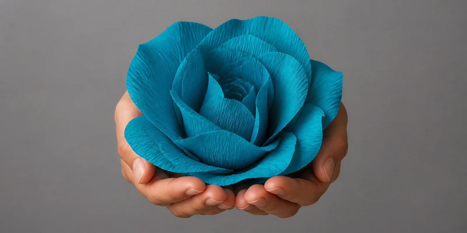 Manos sosteniendo una flor grande de papel crepé celeste mar