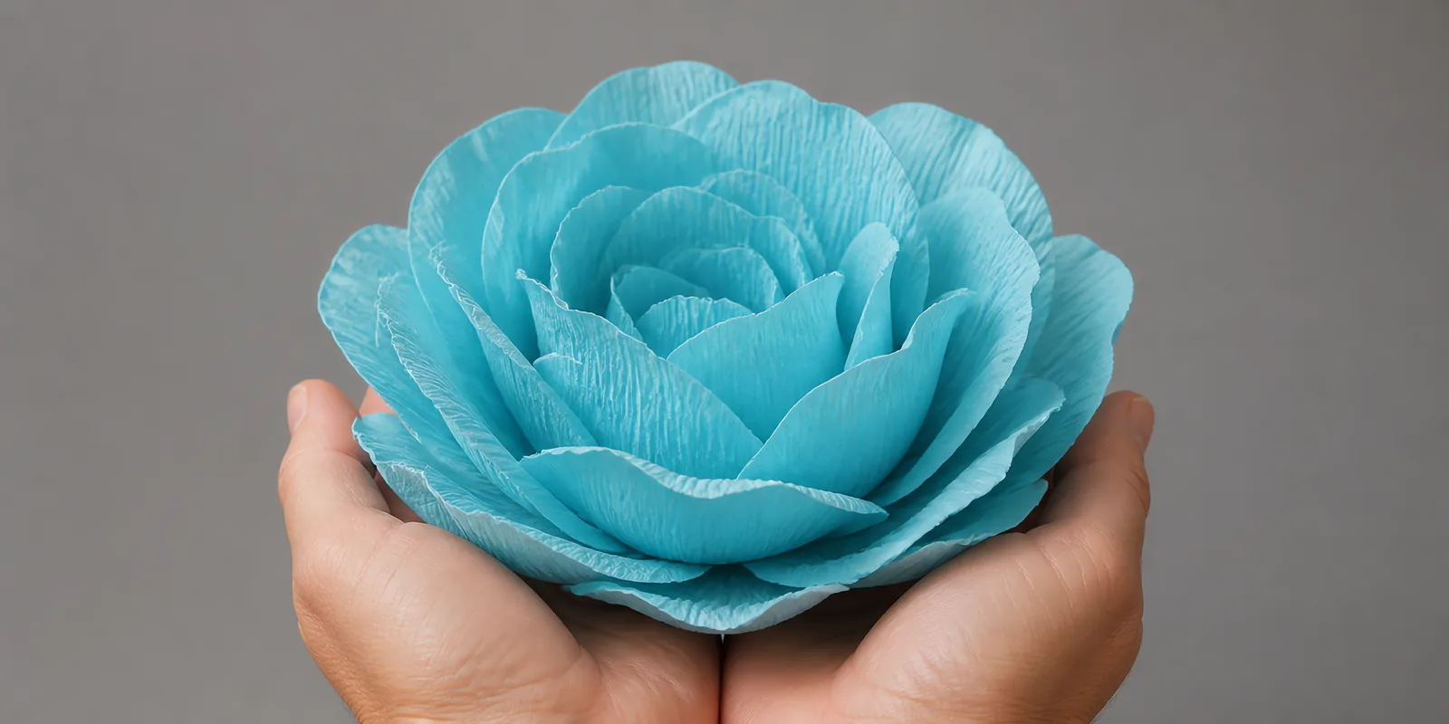 Manos sosteniendo una flor grande de papel crepé celeste pastel