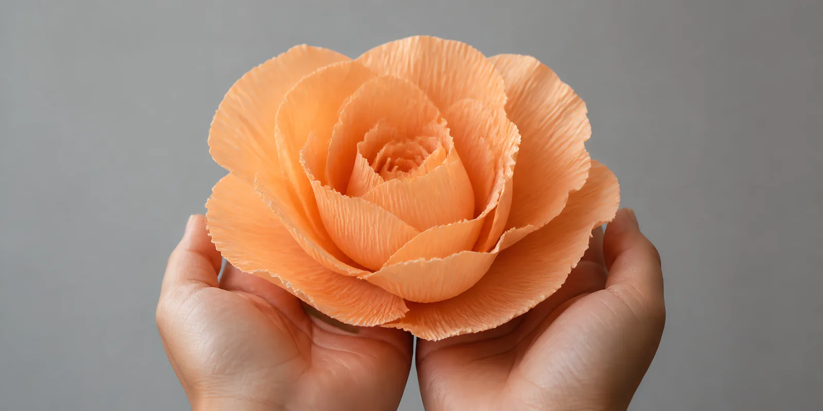Manos sosteniendo una flor grande de papel crepé naranja mandarina