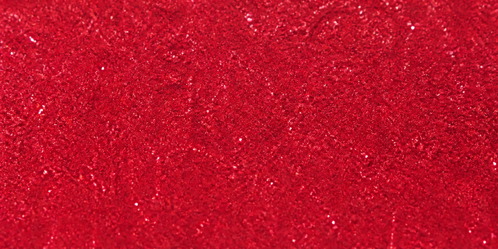 Macro del papel con glitter rojo rosado, con las partículas separadas brillando sobre la hoja