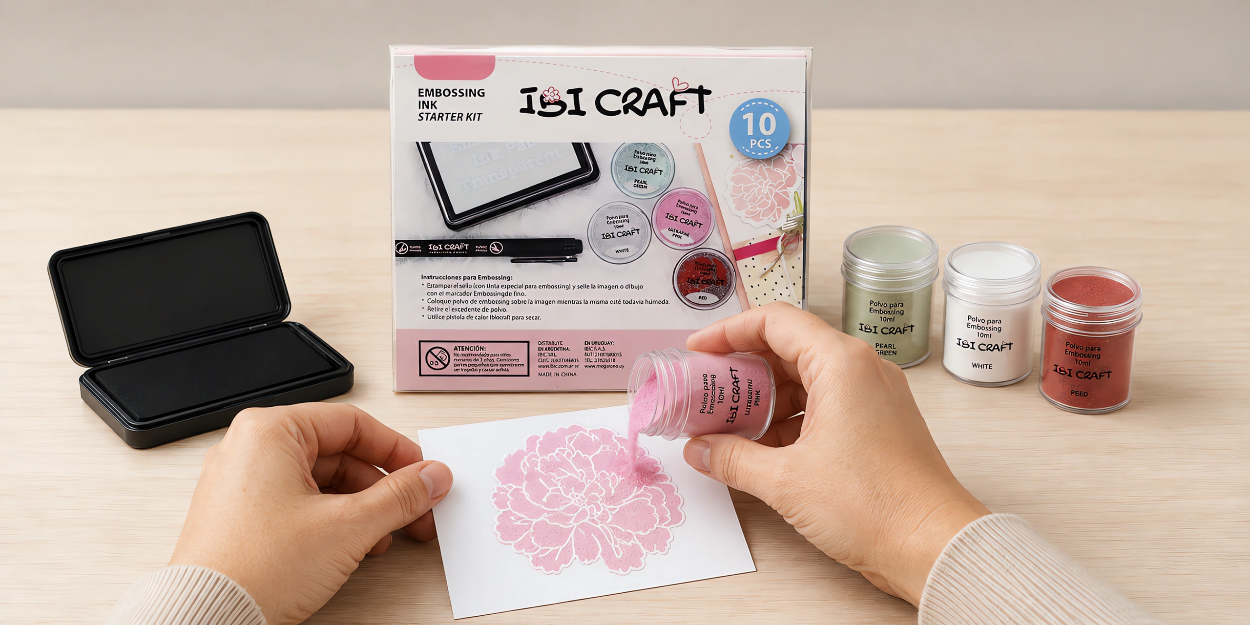 Manos espolvoreando polvo de embossing sobre una imagen recién entintada, con la caja del kit al lado