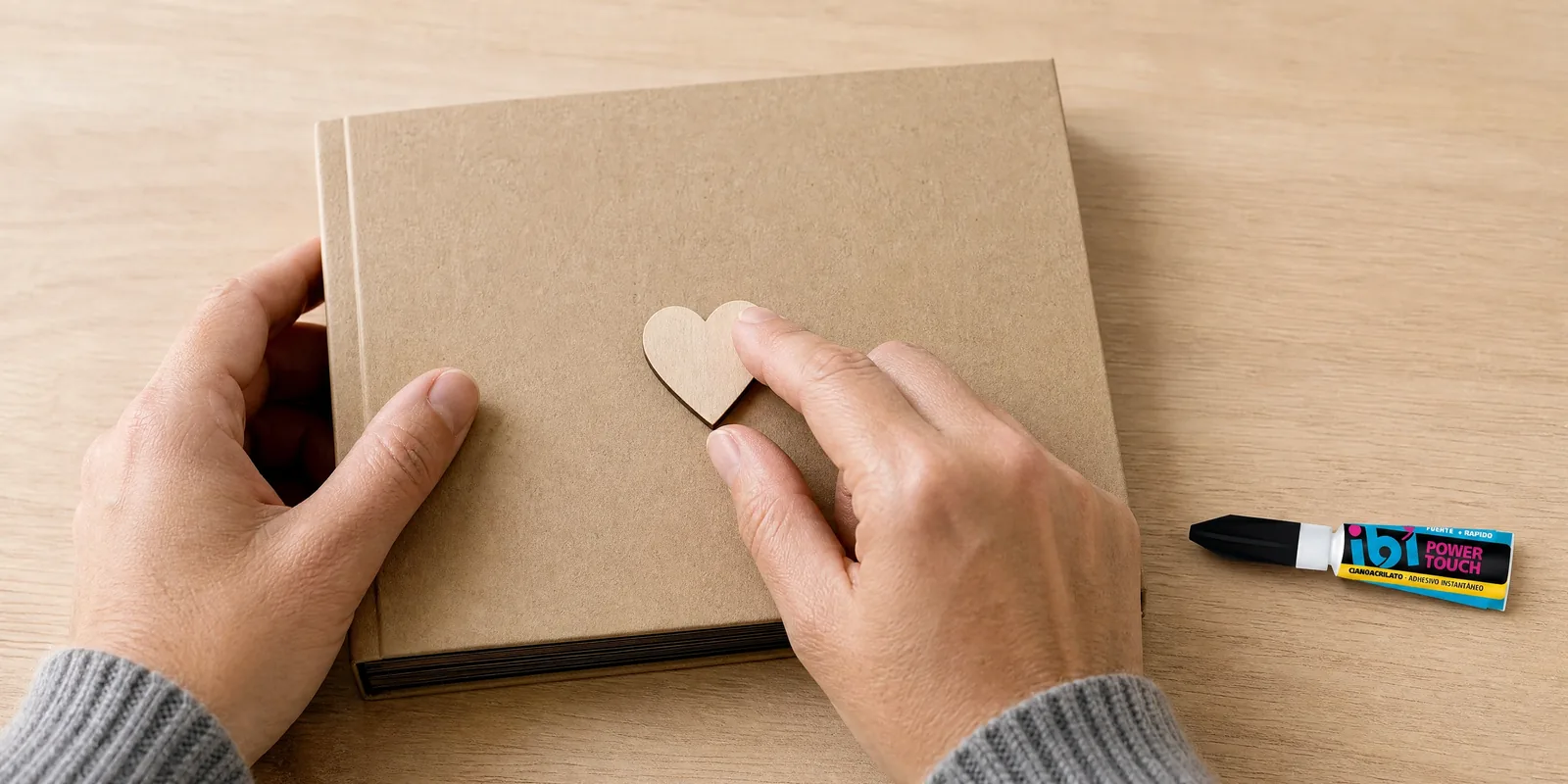 Manos pegando un corazón de madera con el adhesivo instantáneo, con el pomo al lado