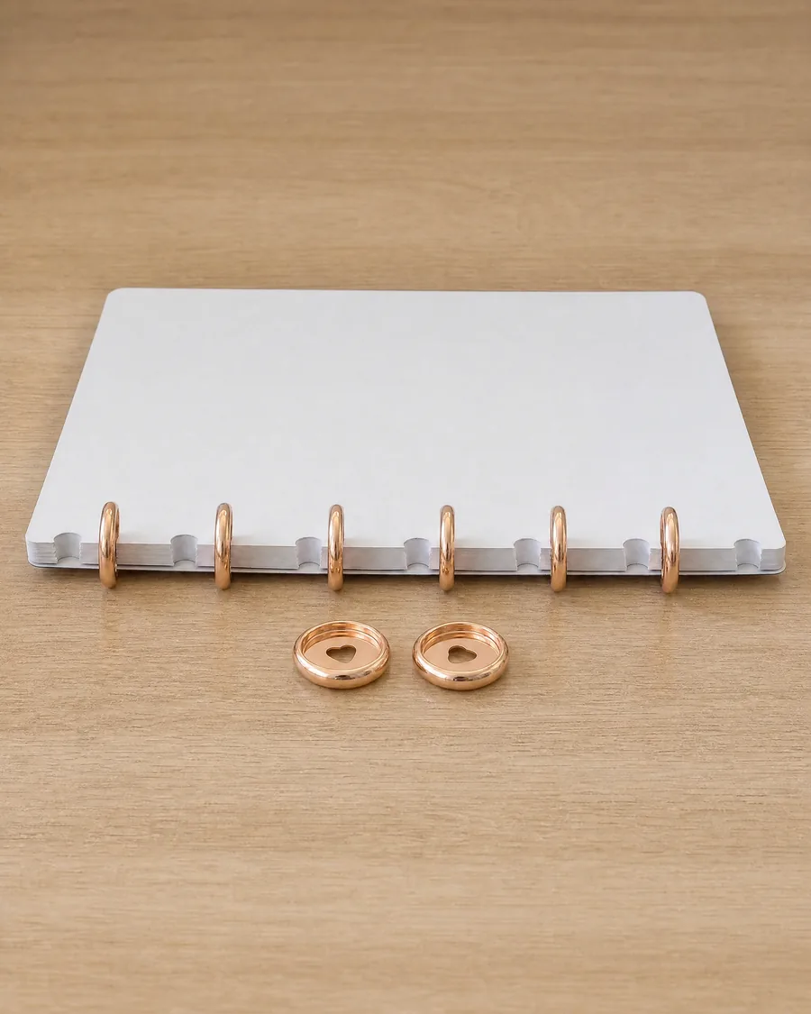 Discos de expansión rosa gold de 24 mm puestos en el lomo de un cuaderno, con dos discos sueltos delante