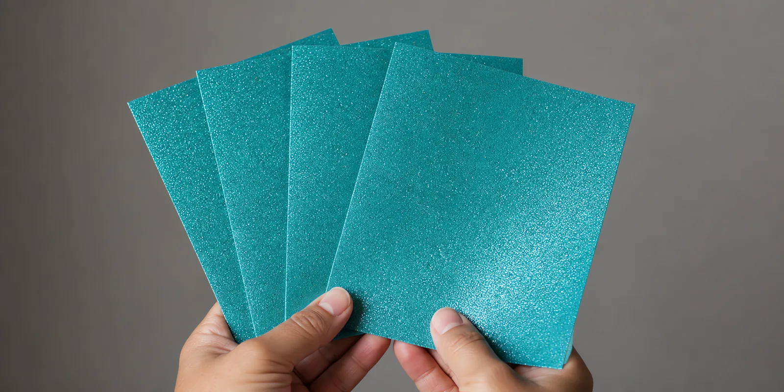 Manos sosteniendo varias hojas de papel con glitter celeste luna de unicornio abiertas en abanico