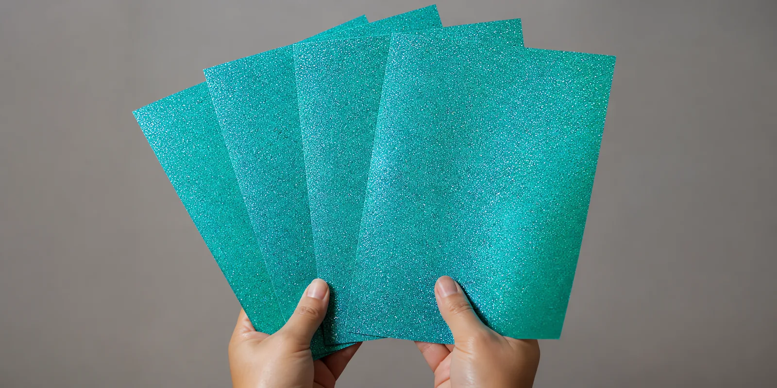 Manos sosteniendo varias hojas de papel con glitter cielo magico abiertas en abanico