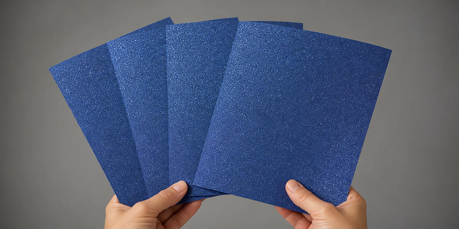 Manos sosteniendo varias hojas de papel con glitter luna azul abiertas en abanico