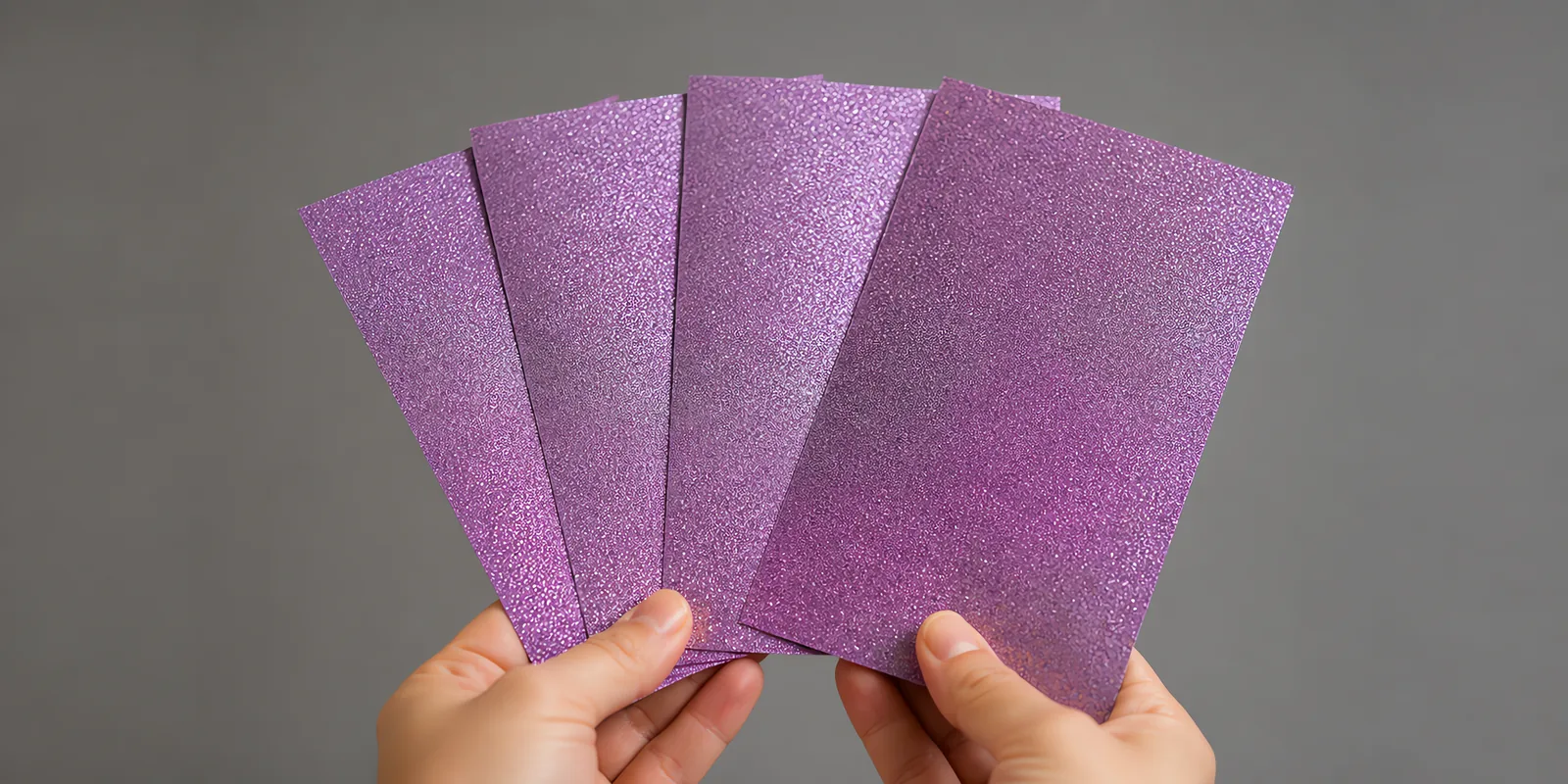 Manos sosteniendo varias hojas de papel con glitter morado mistico abiertas en abanico