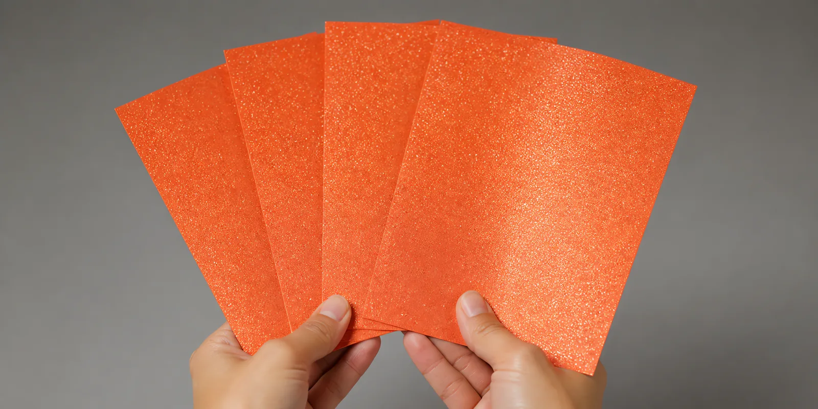 Manos sosteniendo varias hojas de papel con glitter naranja linterna de fuego abiertas en abanico