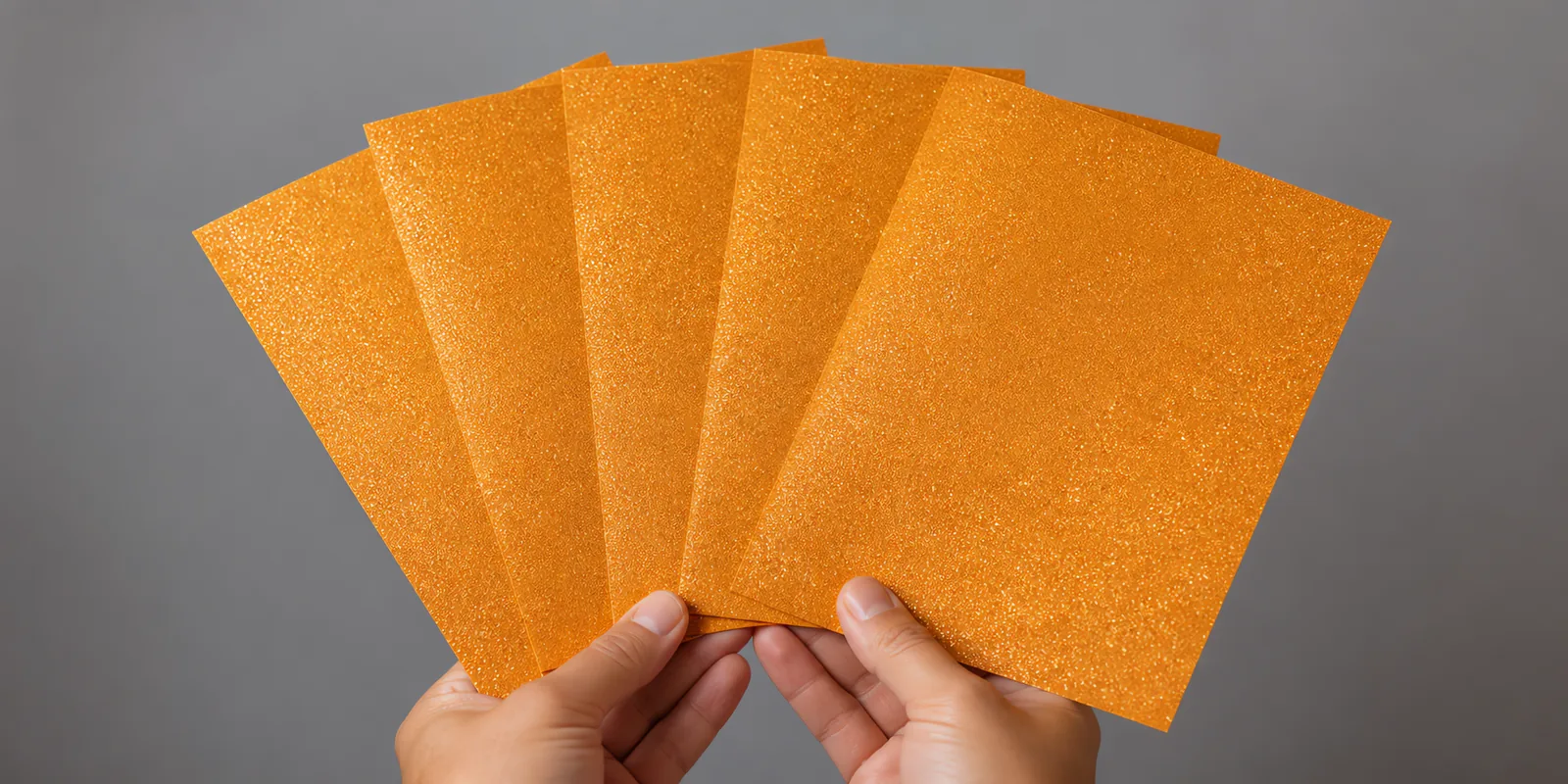 Manos sosteniendo varias hojas de papel con glitter naranja llama encantada abiertas en abanico
