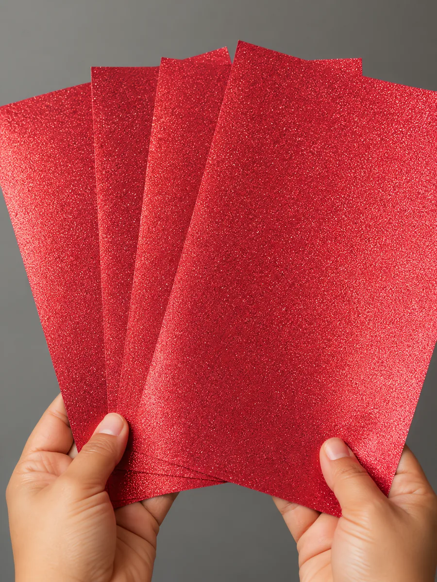 Manos sosteniendo varias hojas de papel con glitter rojo rosado abiertas en abanico