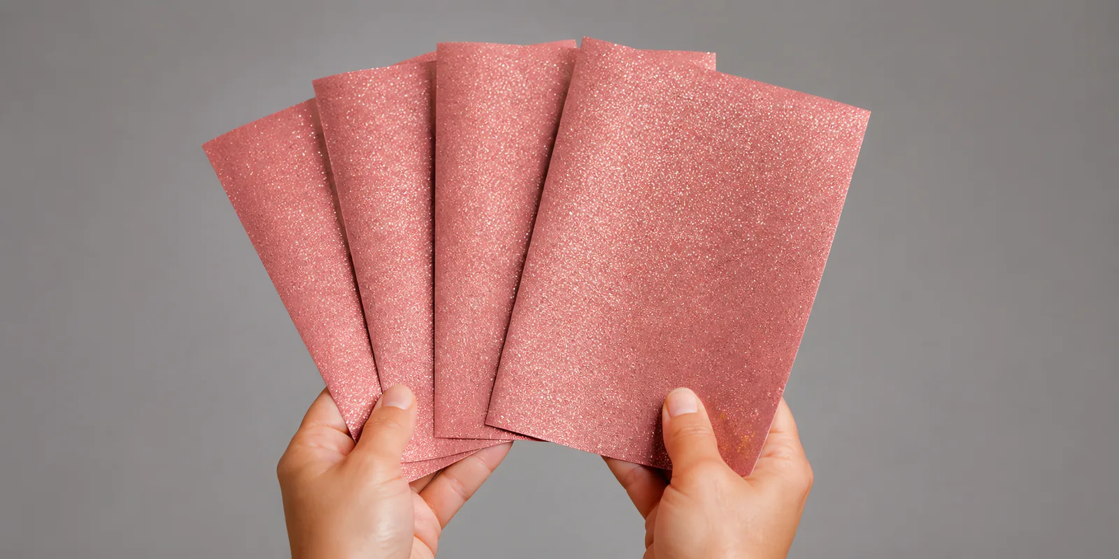 Manos sosteniendo varias hojas de papel con glitter rosa gardenia abiertas en abanico