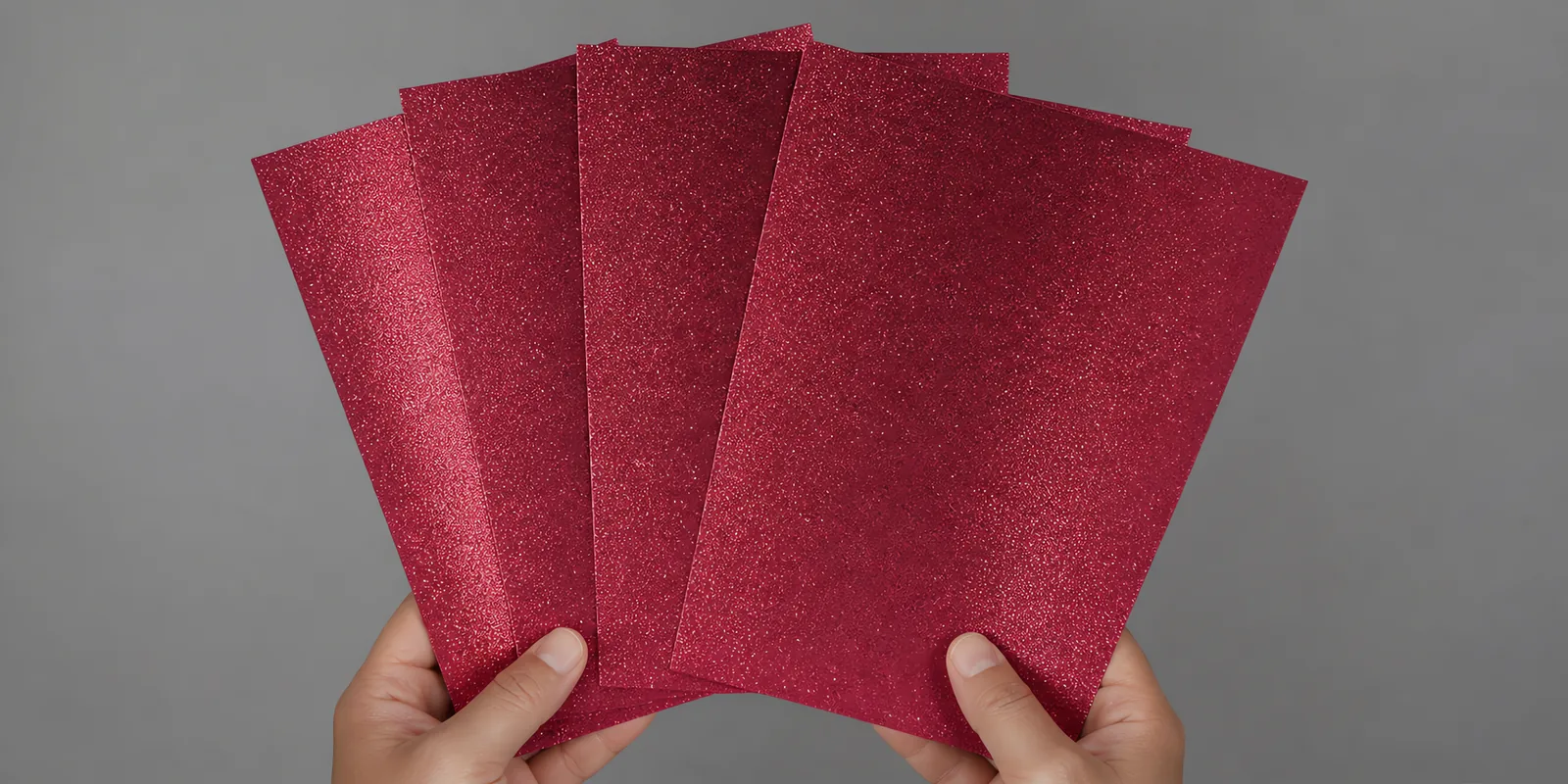 Manos sosteniendo varias hojas de papel con glitter rosa sirena abiertas en abanico