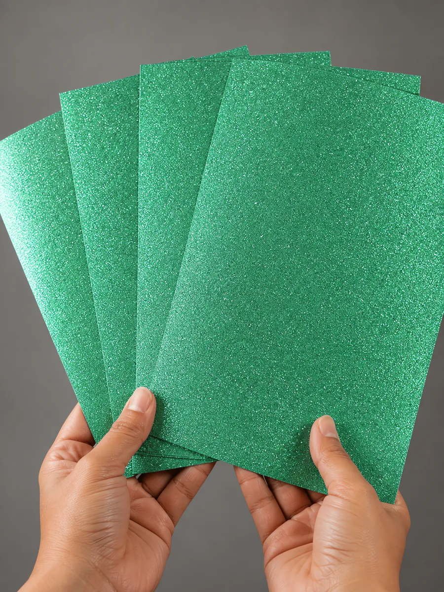 Manos sosteniendo varias hojas de papel con glitter verde alga del mar abiertas en abanico