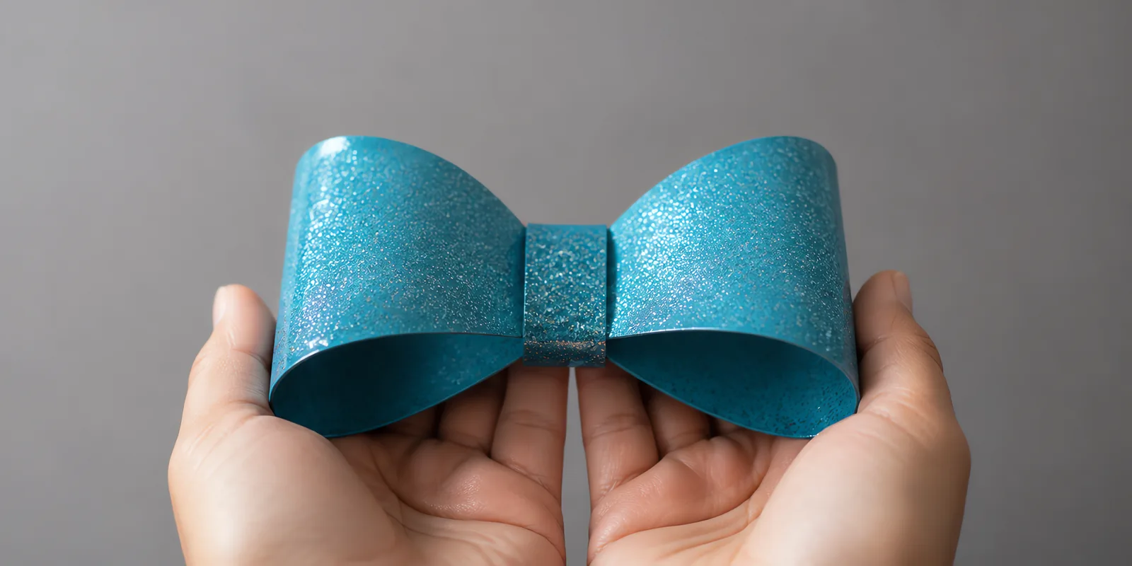 Manos sosteniendo un moño de papel celeste agua con glitter