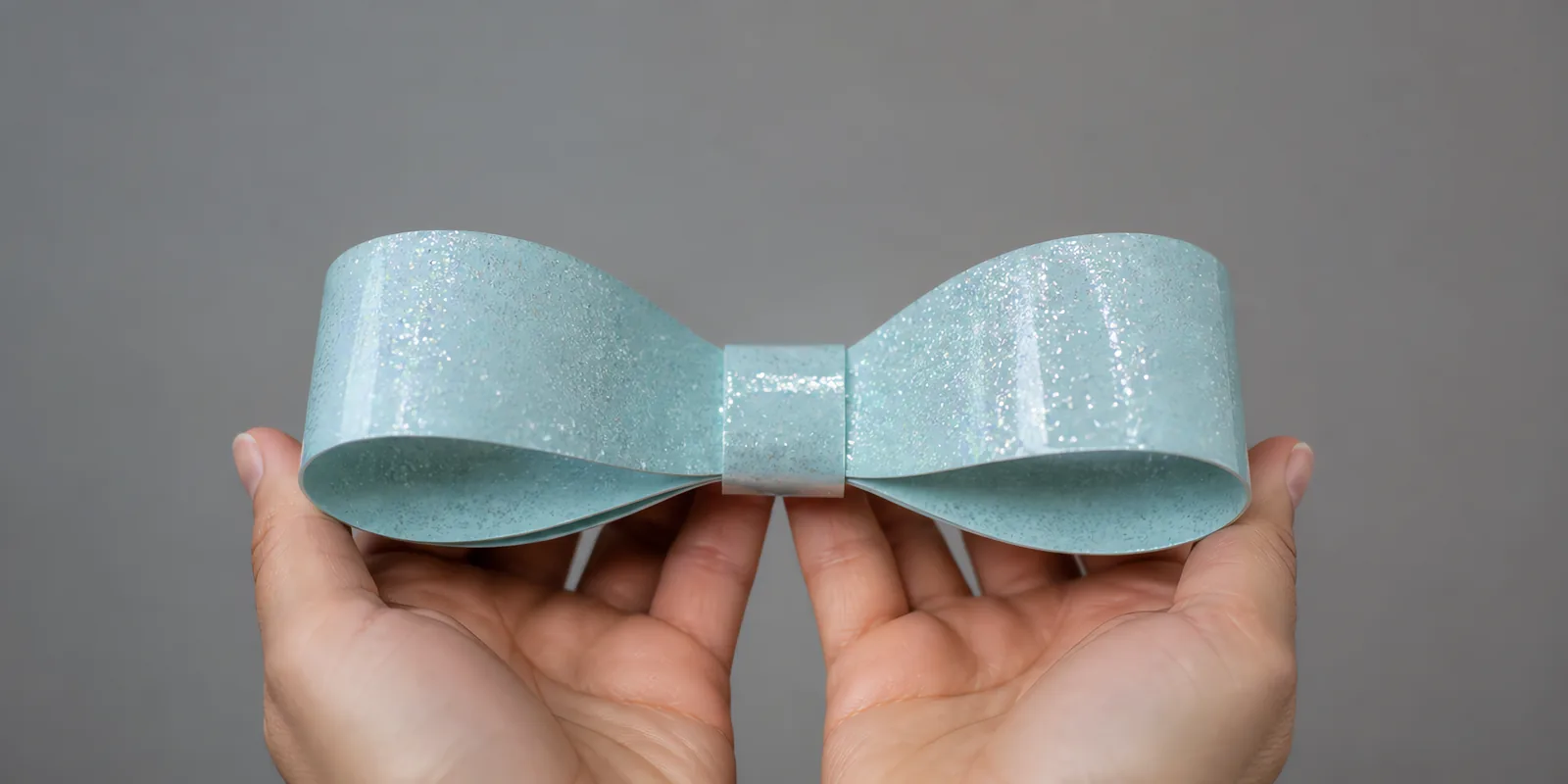 Manos sosteniendo un moño de papel celeste glaciar con glitter