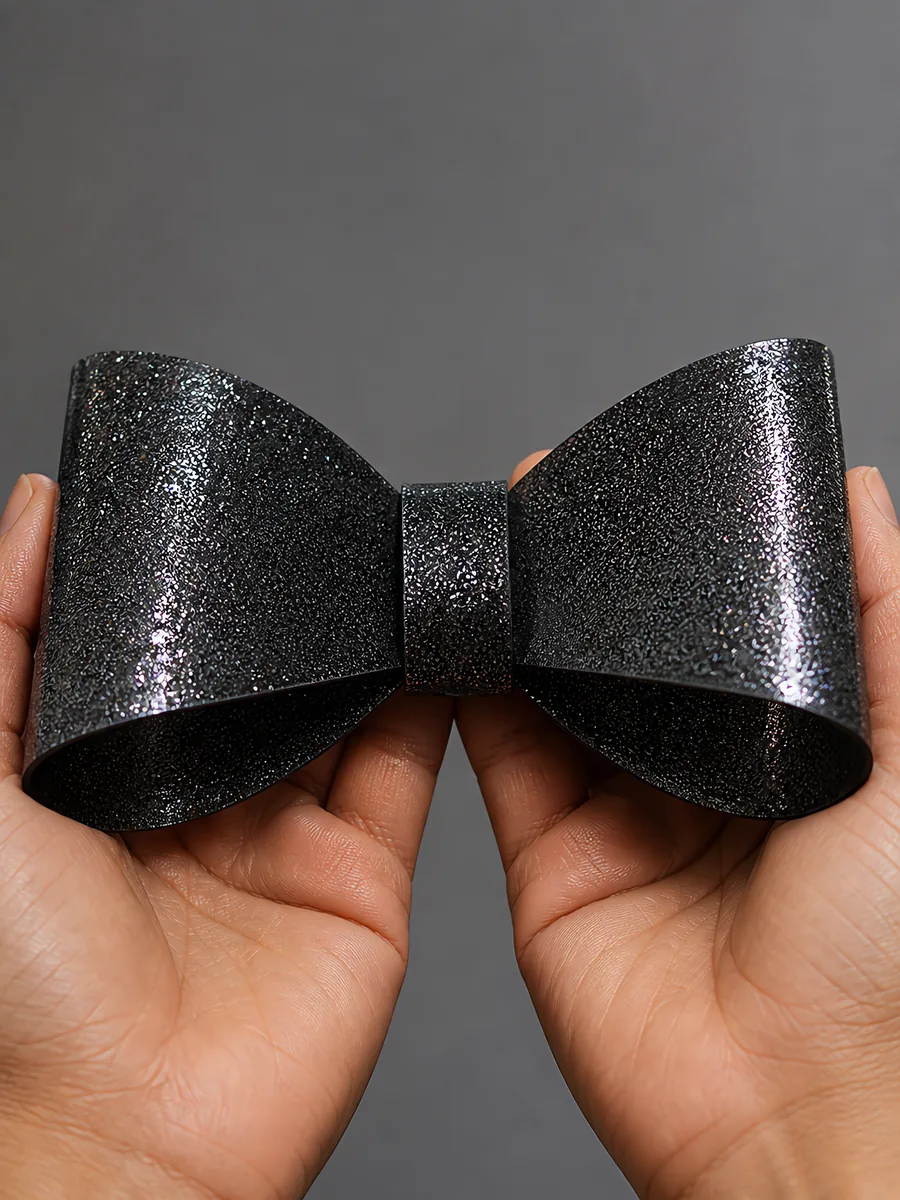 Manos sosteniendo un moño de papel negro noche con glitter