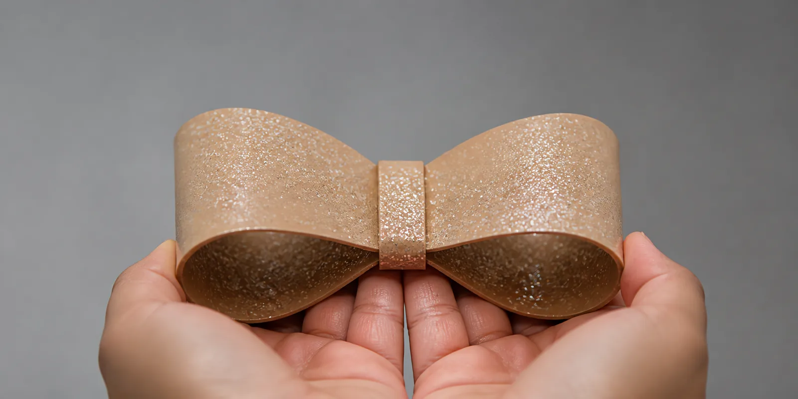 Manos sosteniendo un moño de papel oro beige con glitter