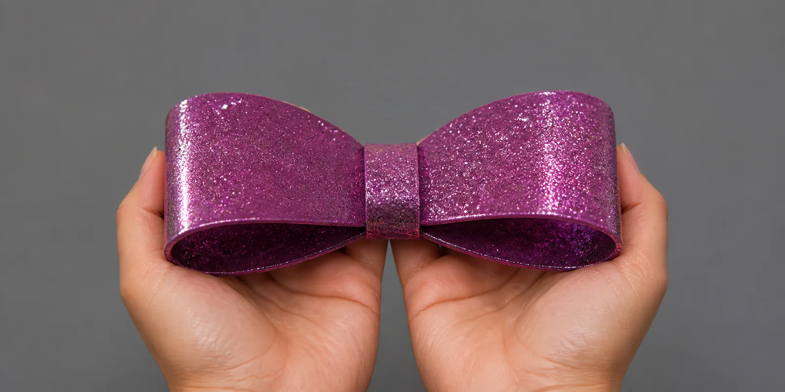 Manos sosteniendo un moño de papel púrpura con glitter