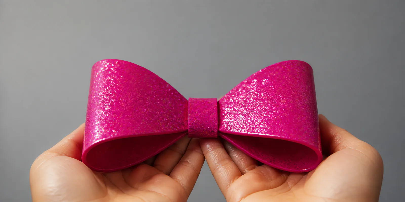 Manos sosteniendo un moño de papel rosa neon con glitter
