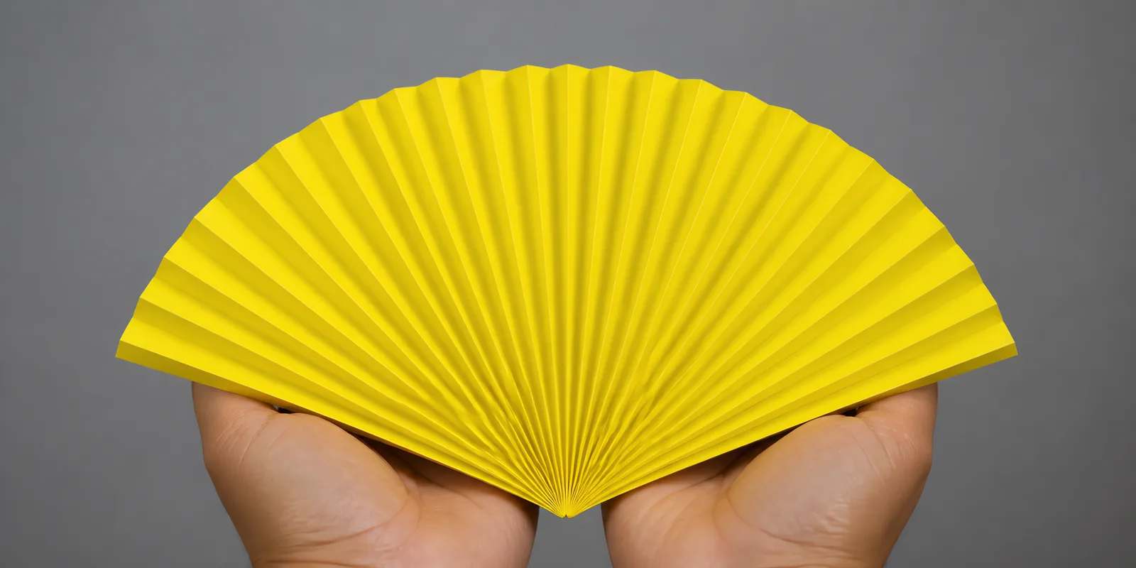 Manos sosteniendo un abanico de papel plegado en acordeón, en amarillo fluor