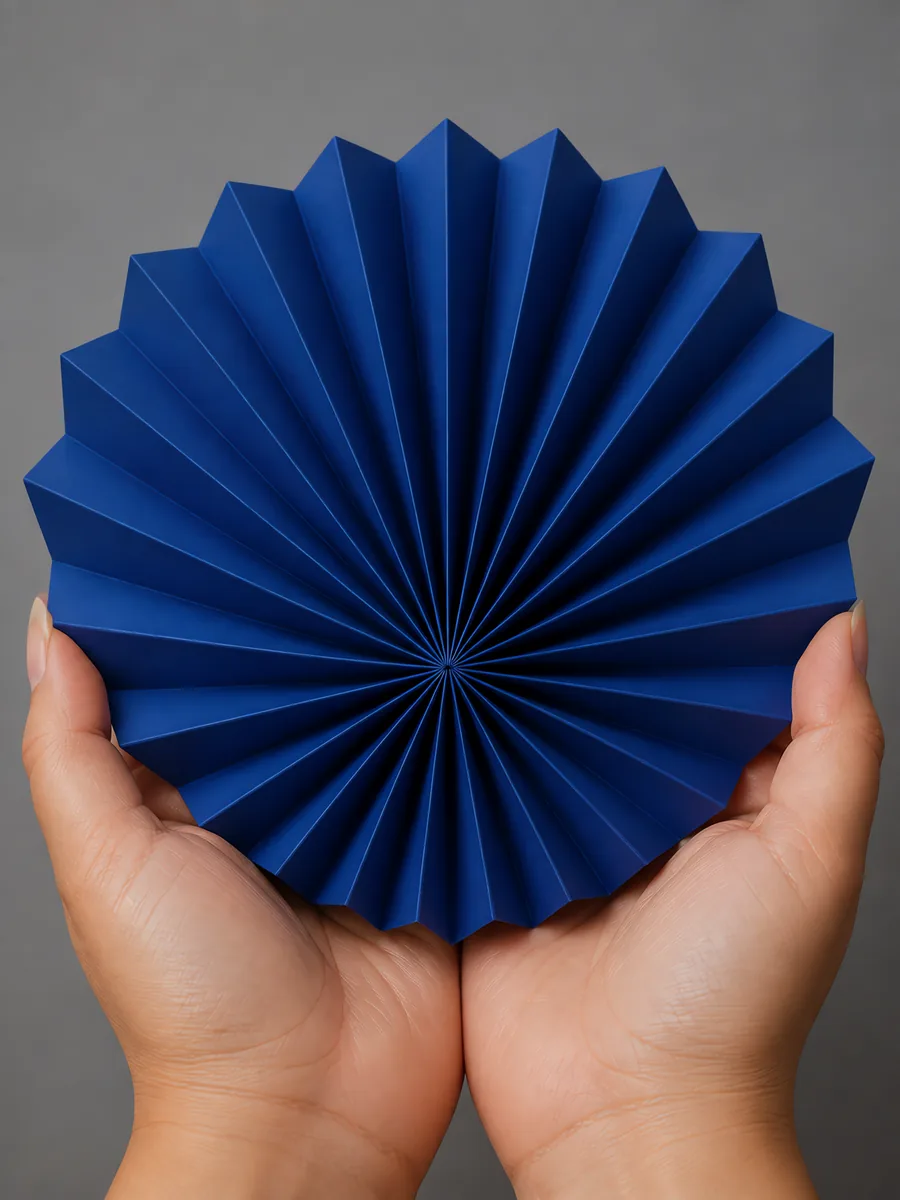 Manos sosteniendo un abanico de papel plegado en acordeón, en azul profundo