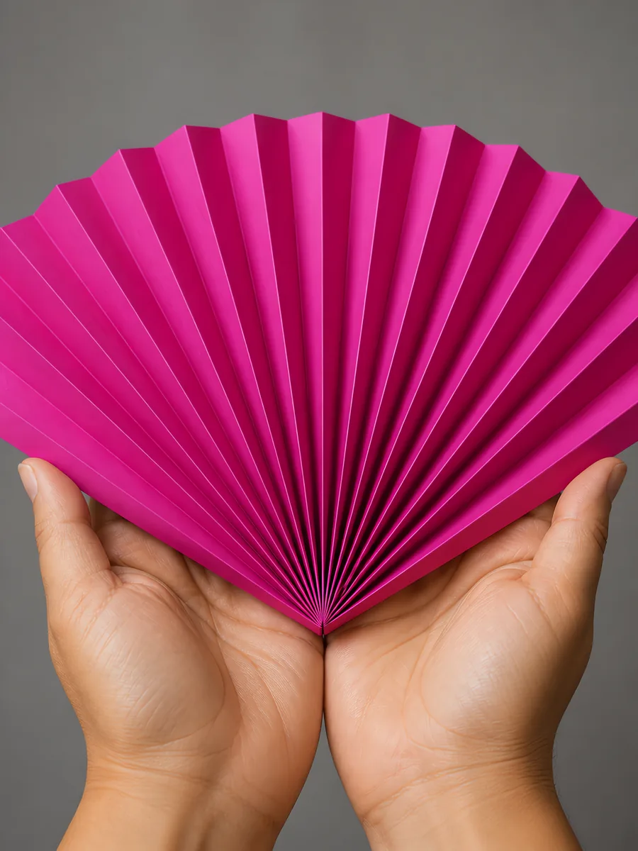 Manos sosteniendo un abanico de papel plegado en acordeón, en fucsia chic