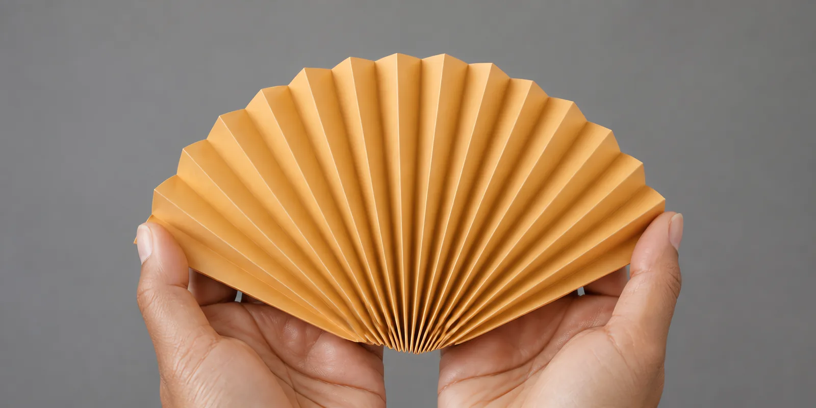 Manos sosteniendo un abanico de papel plegado en acordeón, en naranja fluo