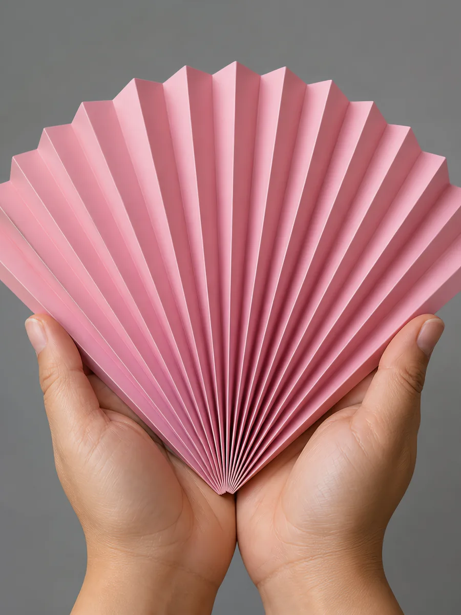 Manos sosteniendo un abanico de papel plegado en acordeón, en rosa fluo