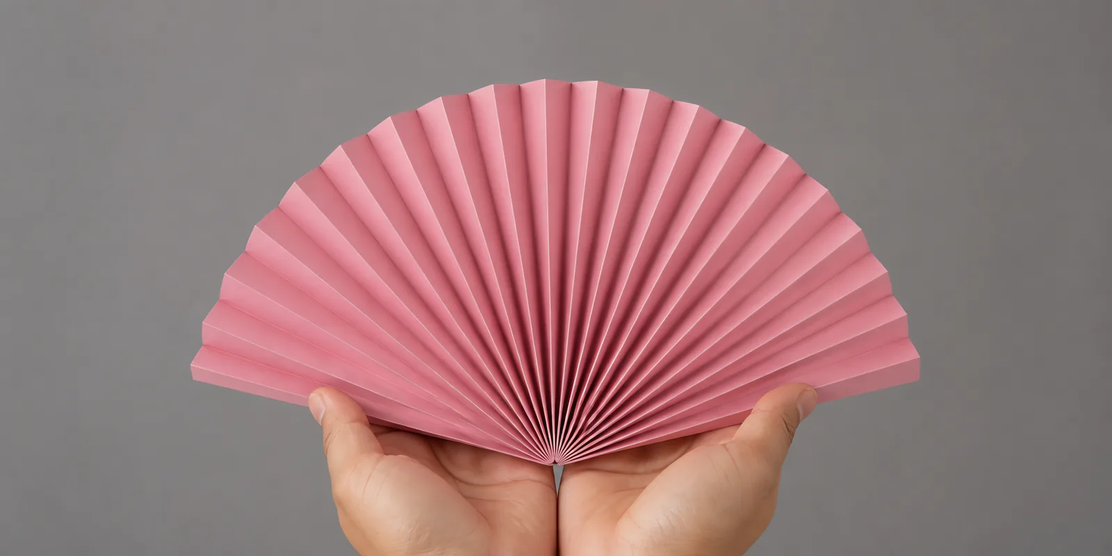 Manos sosteniendo un abanico de papel plegado en acordeón, en rosa fluo