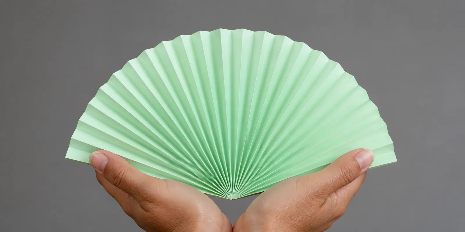 Manos sosteniendo un abanico de papel plegado en acordeón, en verde pastel