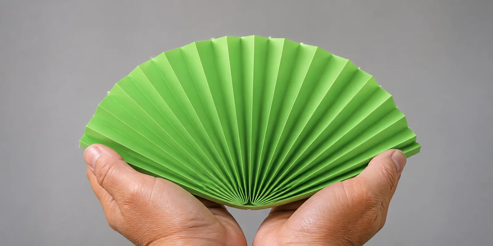 Manos sosteniendo un abanico de papel plegado en acordeón, en verde primavera