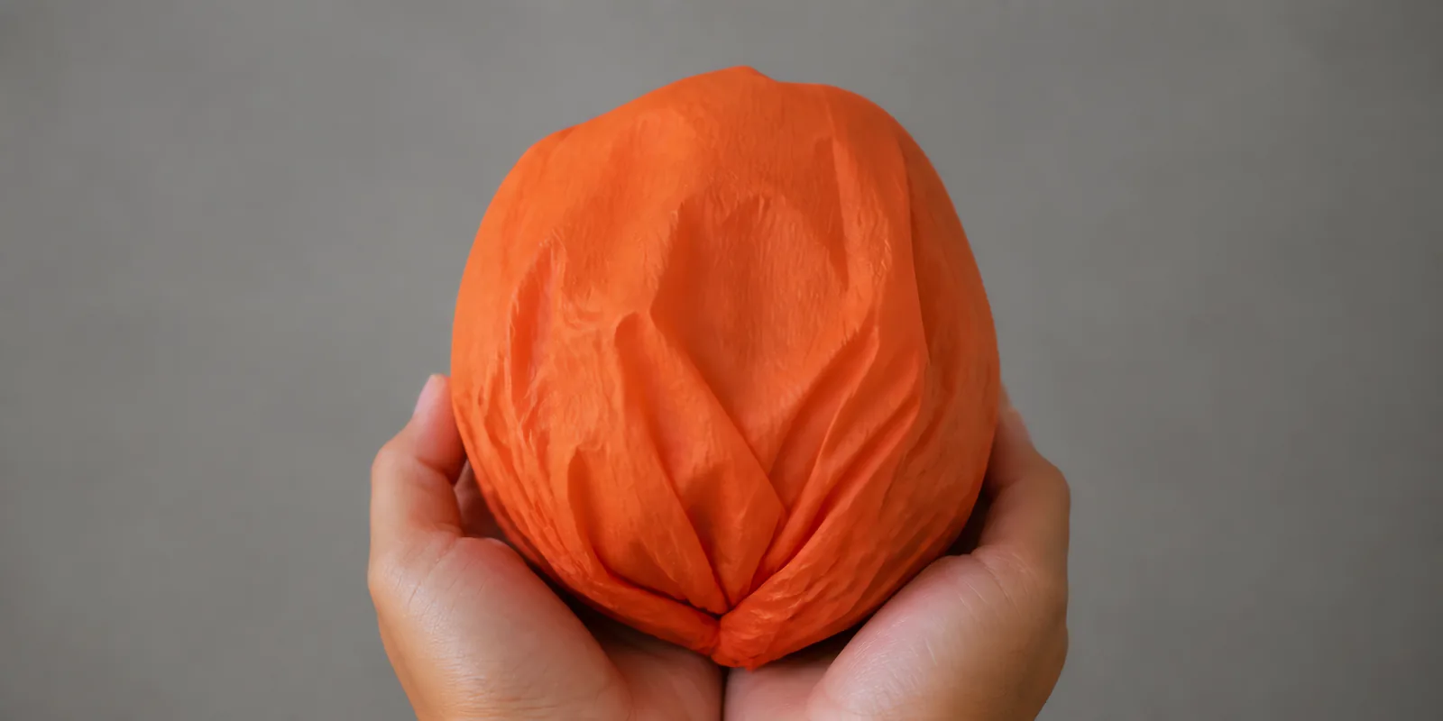 Manos sosteniendo desde abajo un envoltorio de papel seda naranja