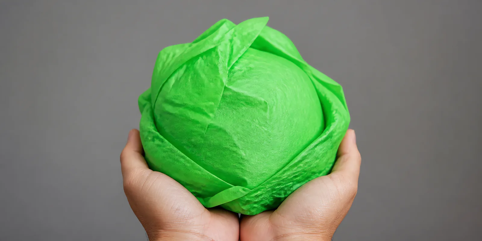 Manos sosteniendo desde abajo un envoltorio de papel seda verde fluor
