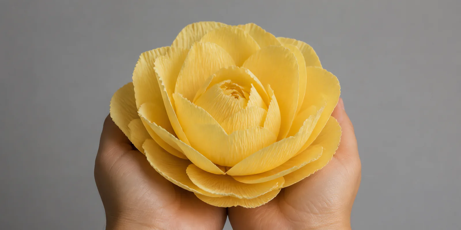 Manos sosteniendo una flor grande de papel crepé amarillo girasol