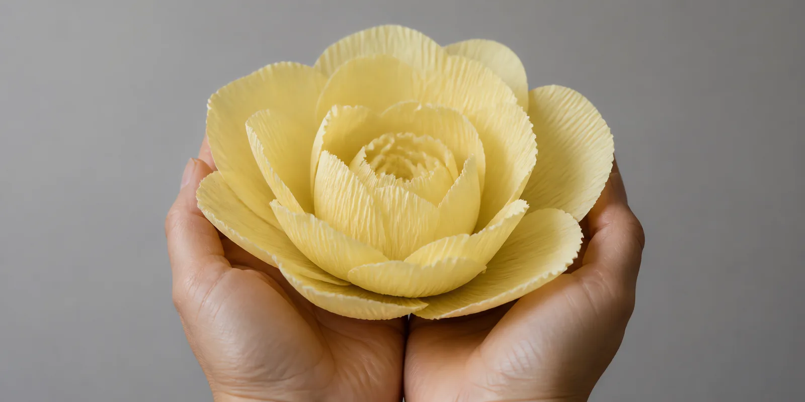 Manos sosteniendo una flor grande de papel crepé amarillo pastel