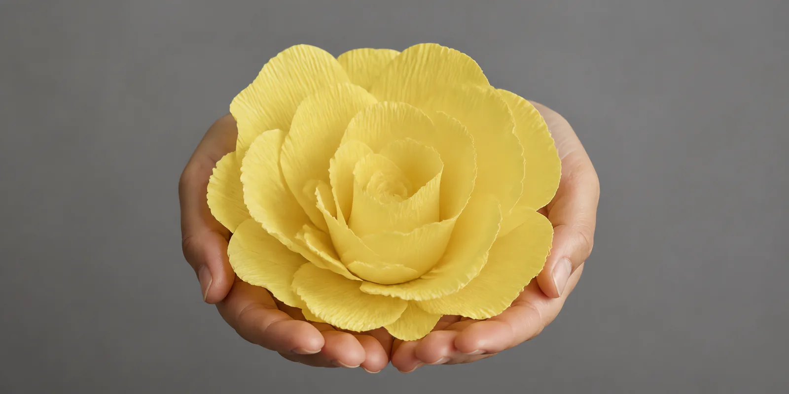 Manos sosteniendo una flor grande de papel crepé amarillo patito