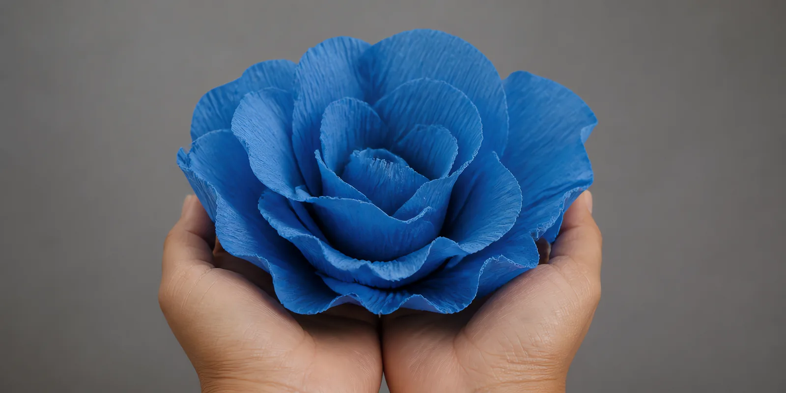 Manos sosteniendo una flor grande de papel crepé azul cielo
