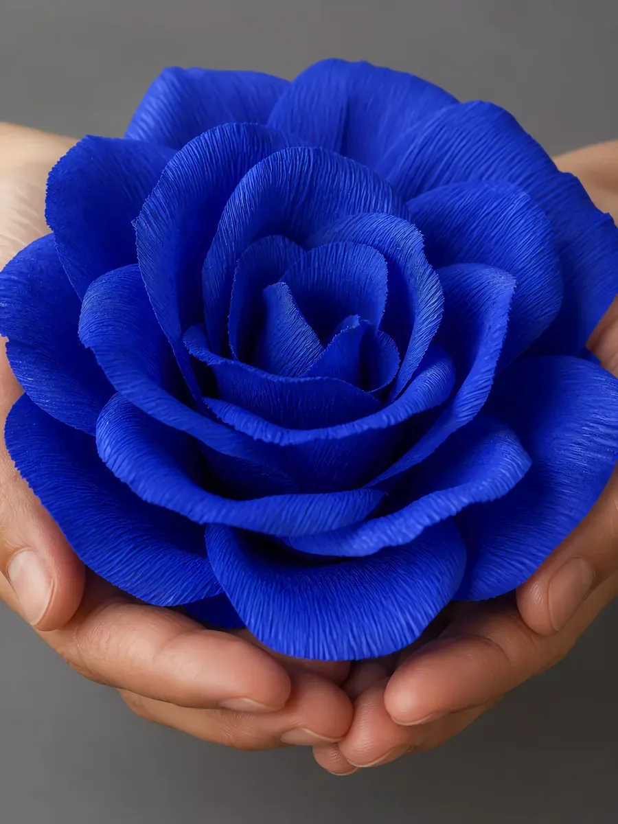 Manos sosteniendo una flor grande de papel crepé azul cósmico