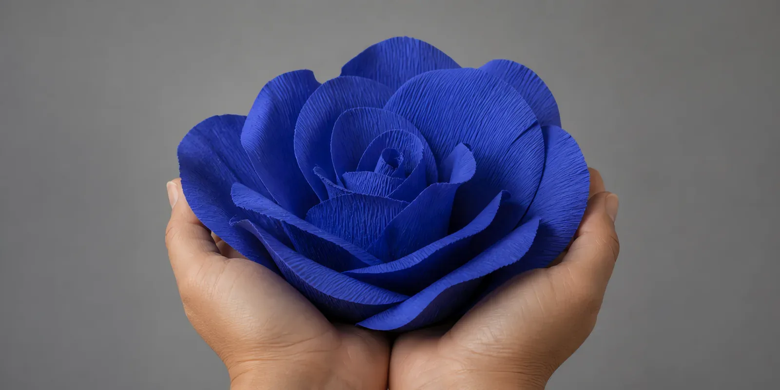 Manos sosteniendo una flor grande de papel crepé azul cósmico