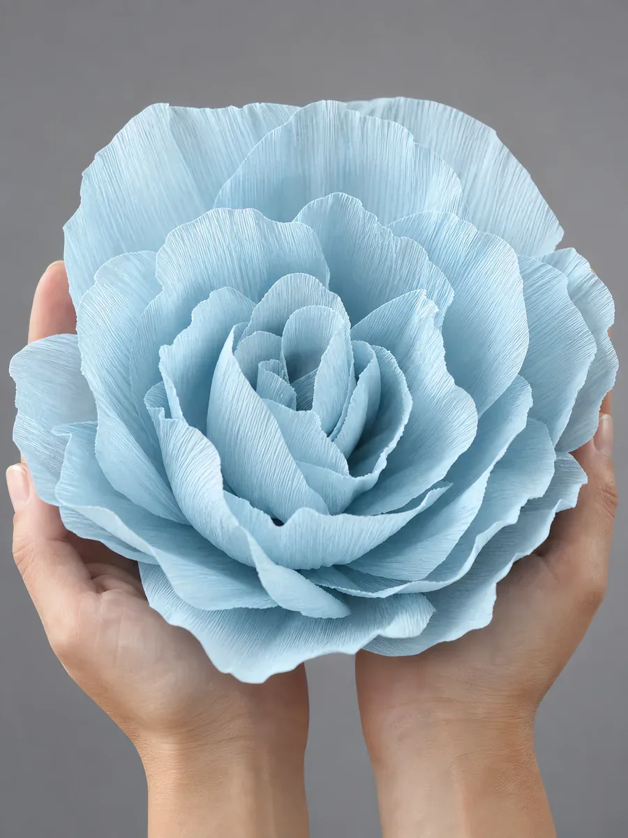 Manos sosteniendo una flor grande de papel crepé celeste cielo