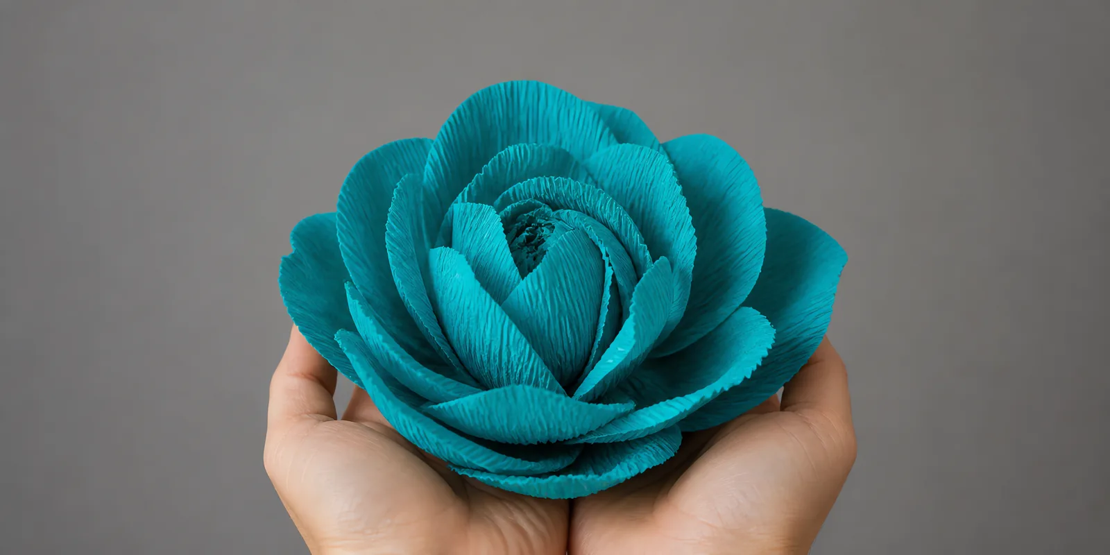 Manos sosteniendo una flor grande de papel crepé celeste encantado