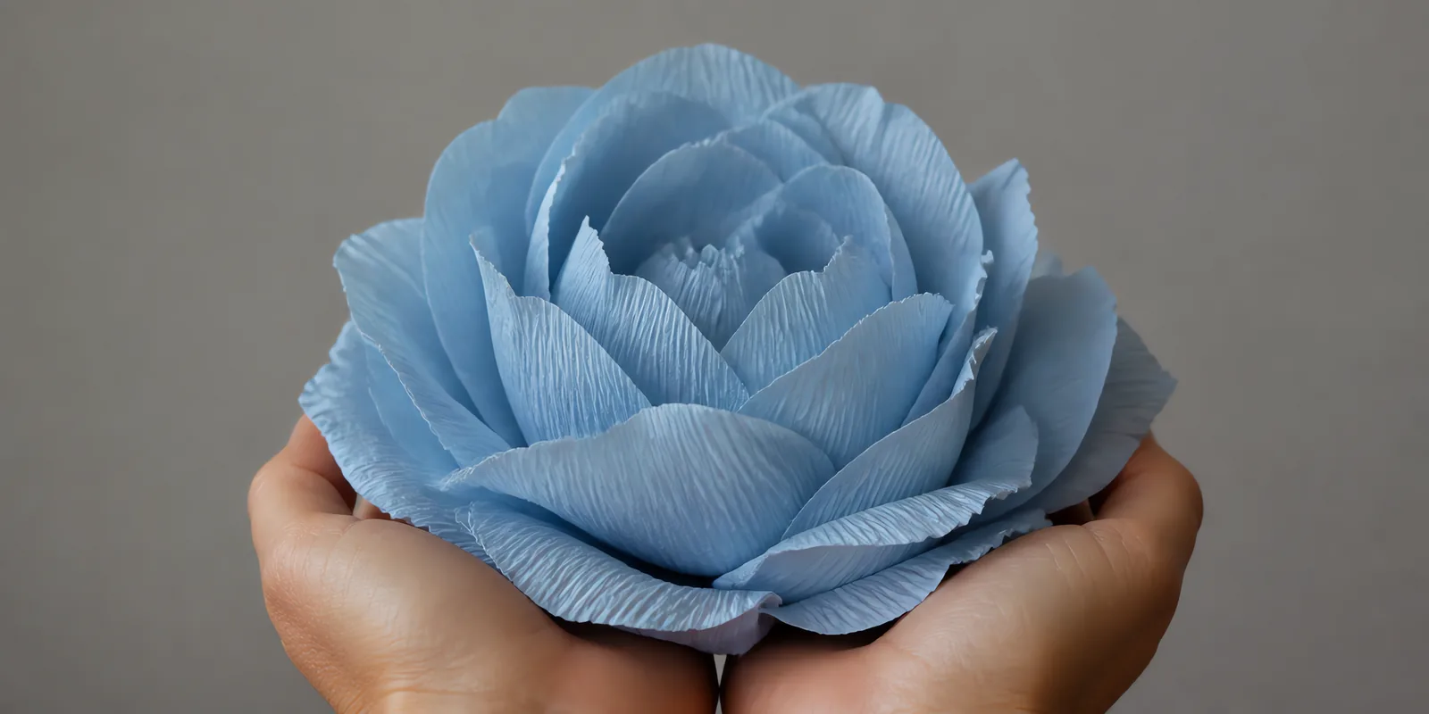 Manos sosteniendo una flor grande de papel crepé celeste sereno