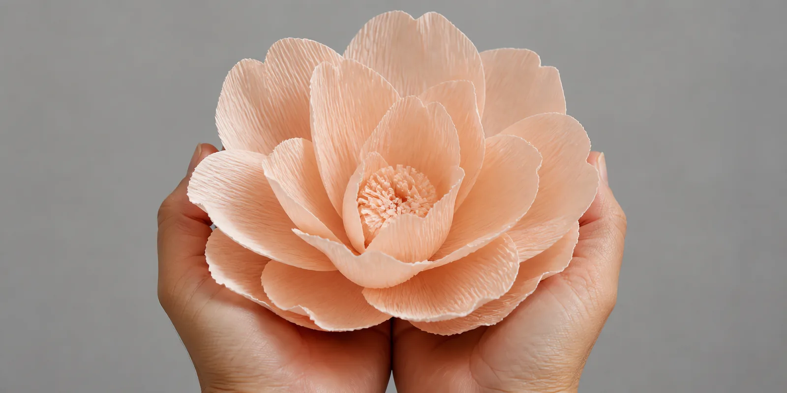 Manos sosteniendo una flor grande de papel crepé coral pastel