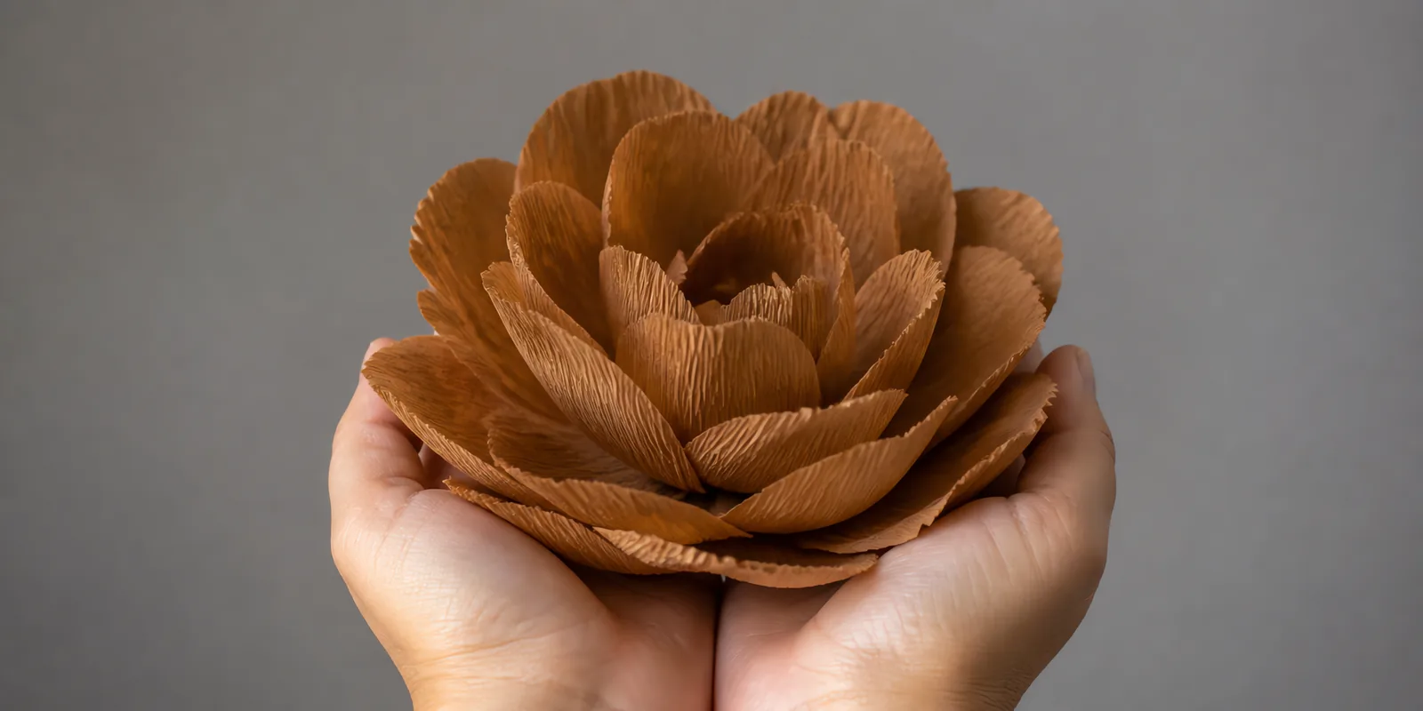 Manos sosteniendo una flor grande de papel crepé marrón clarito