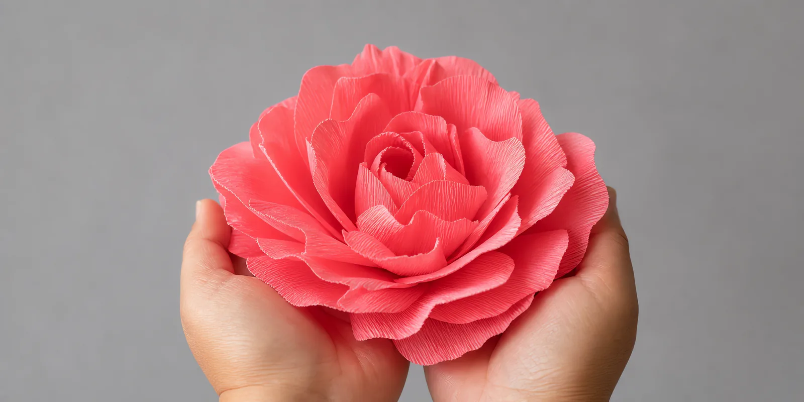 Manos sosteniendo una flor grande de papel crepé rosa melocotón