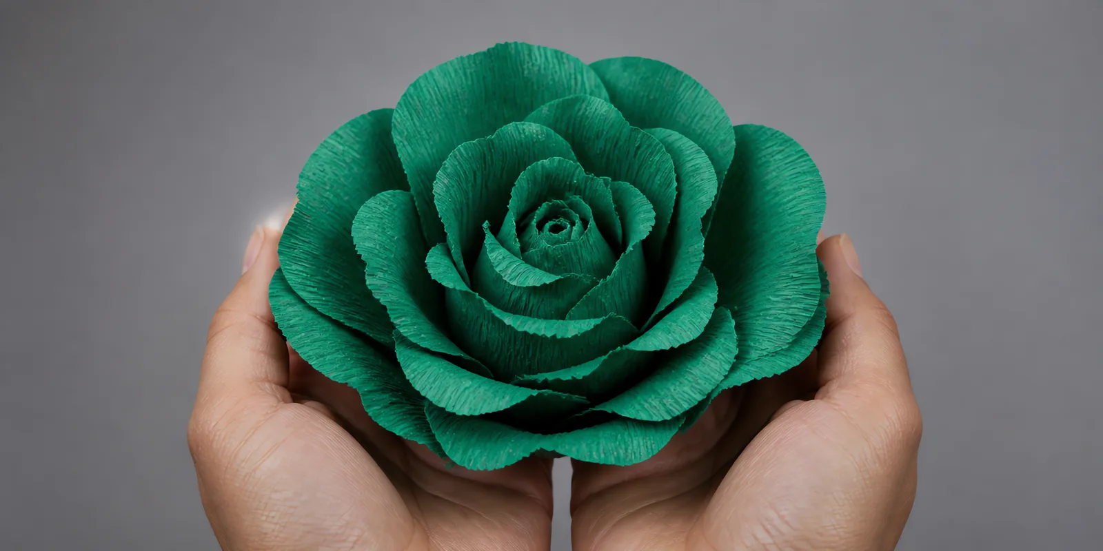 Manos sosteniendo una flor grande de papel crepé verde esmeralda