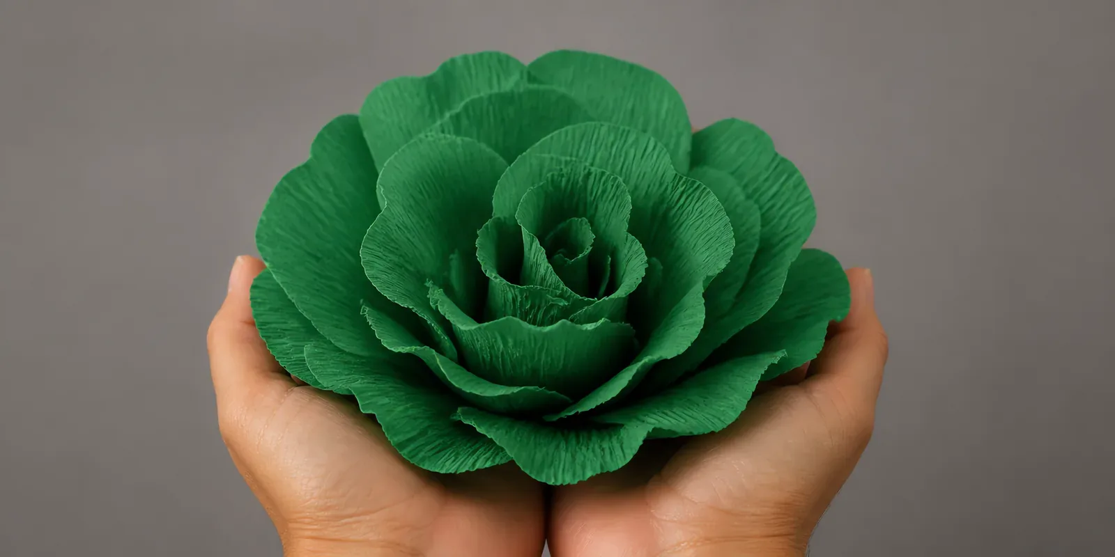 Manos sosteniendo una flor grande de papel crepé verde pasto