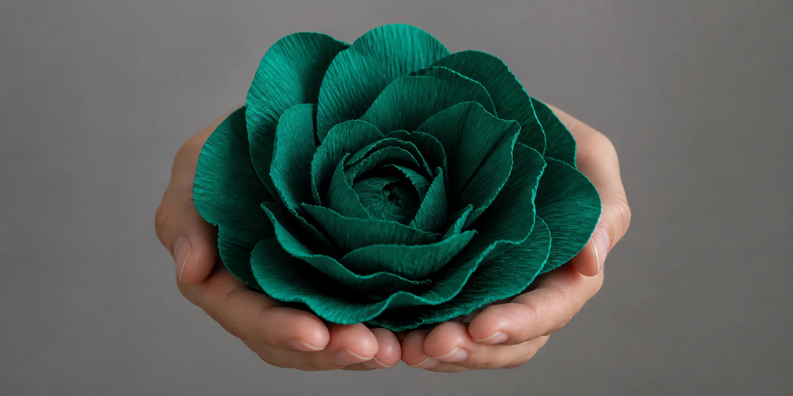 Manos sosteniendo una flor grande de papel crepé verde petróleo
